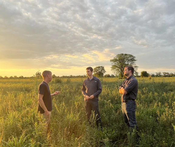 Tres hombres conversando en un campo al atardecer